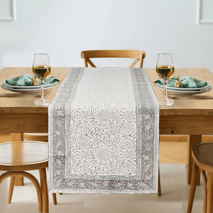 Dining table set with a patterned table runner, glasses, and plates.