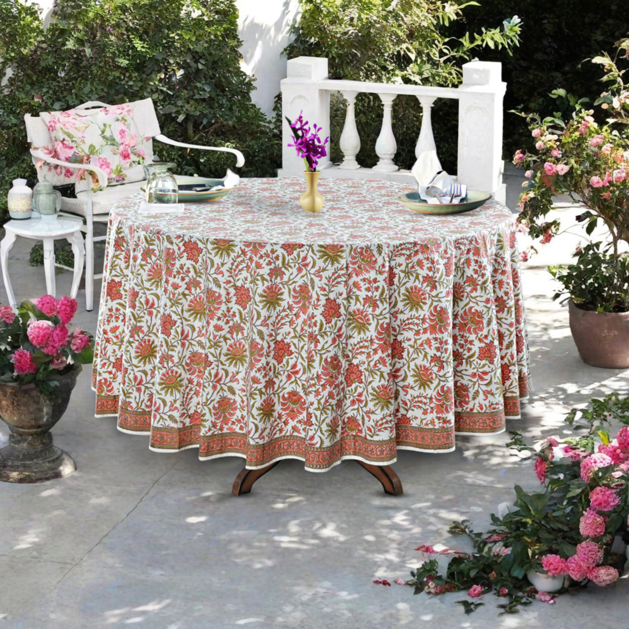Round table with a floral tablecloth in an outdoor setting with chairs and flowers.