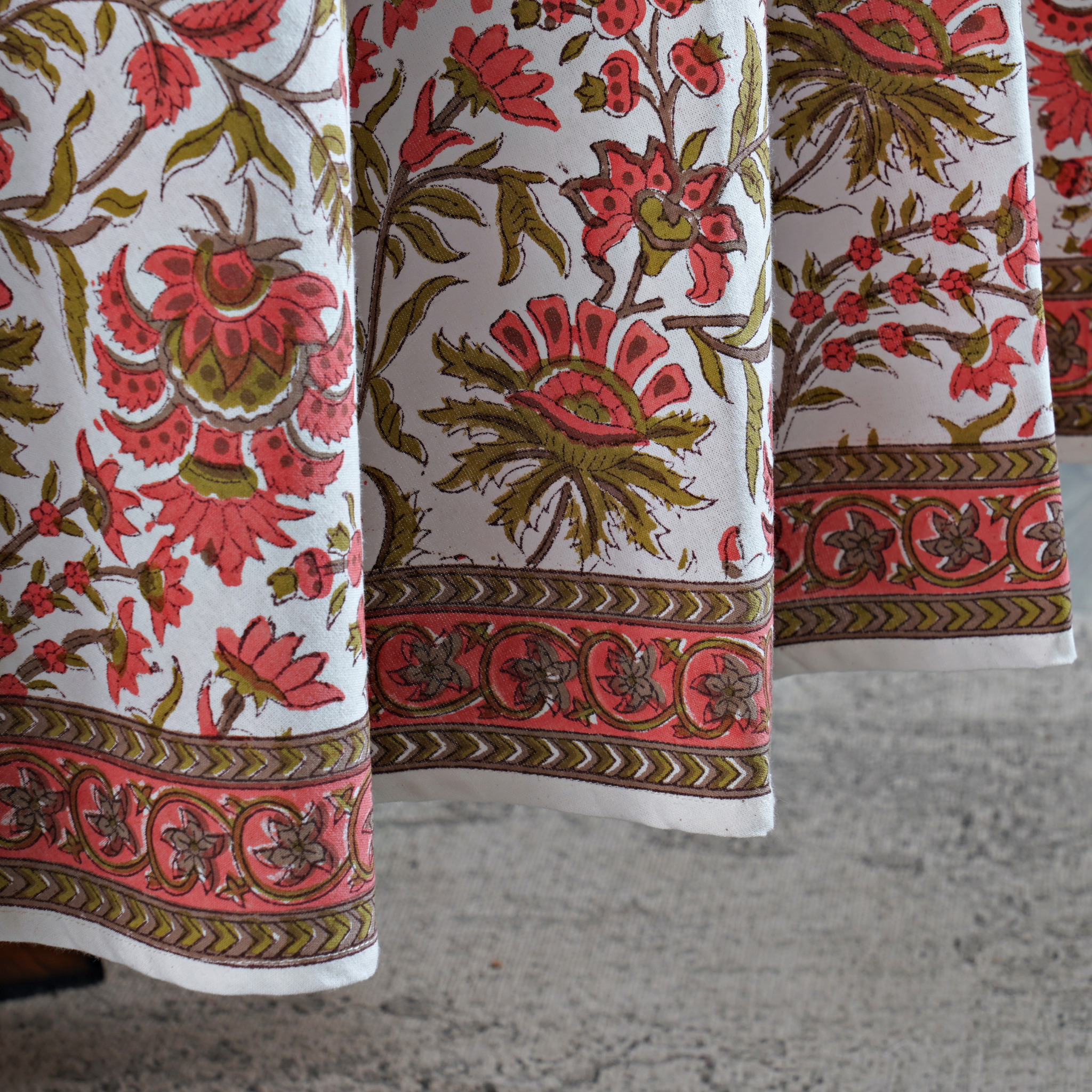 Close-up of a floral patterned fabric with red and green colors on a white background.