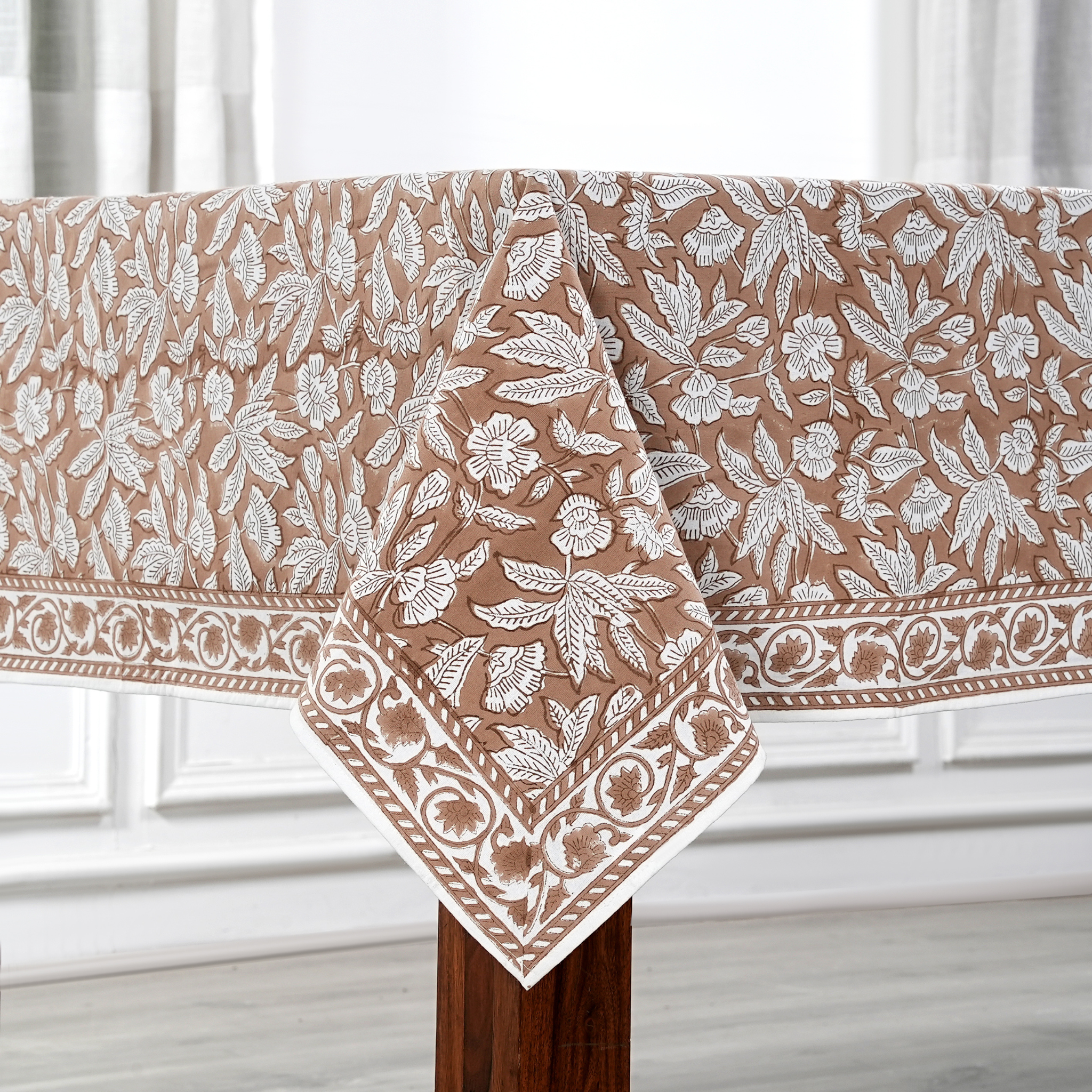 Floral patterned tablecloth on a wooden table with a white curtain background