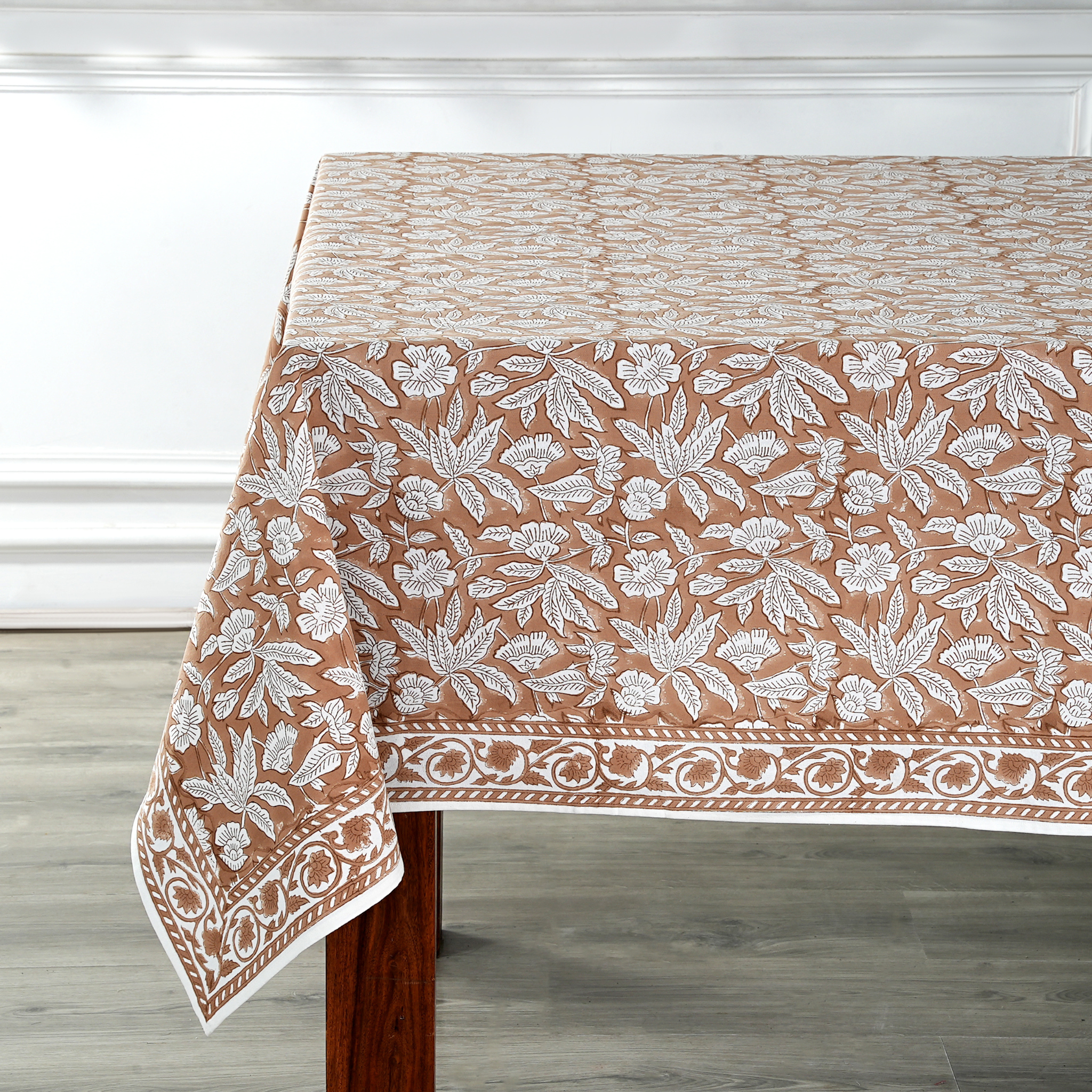 Tablecloth with floral pattern on a wooden table against a white wall.