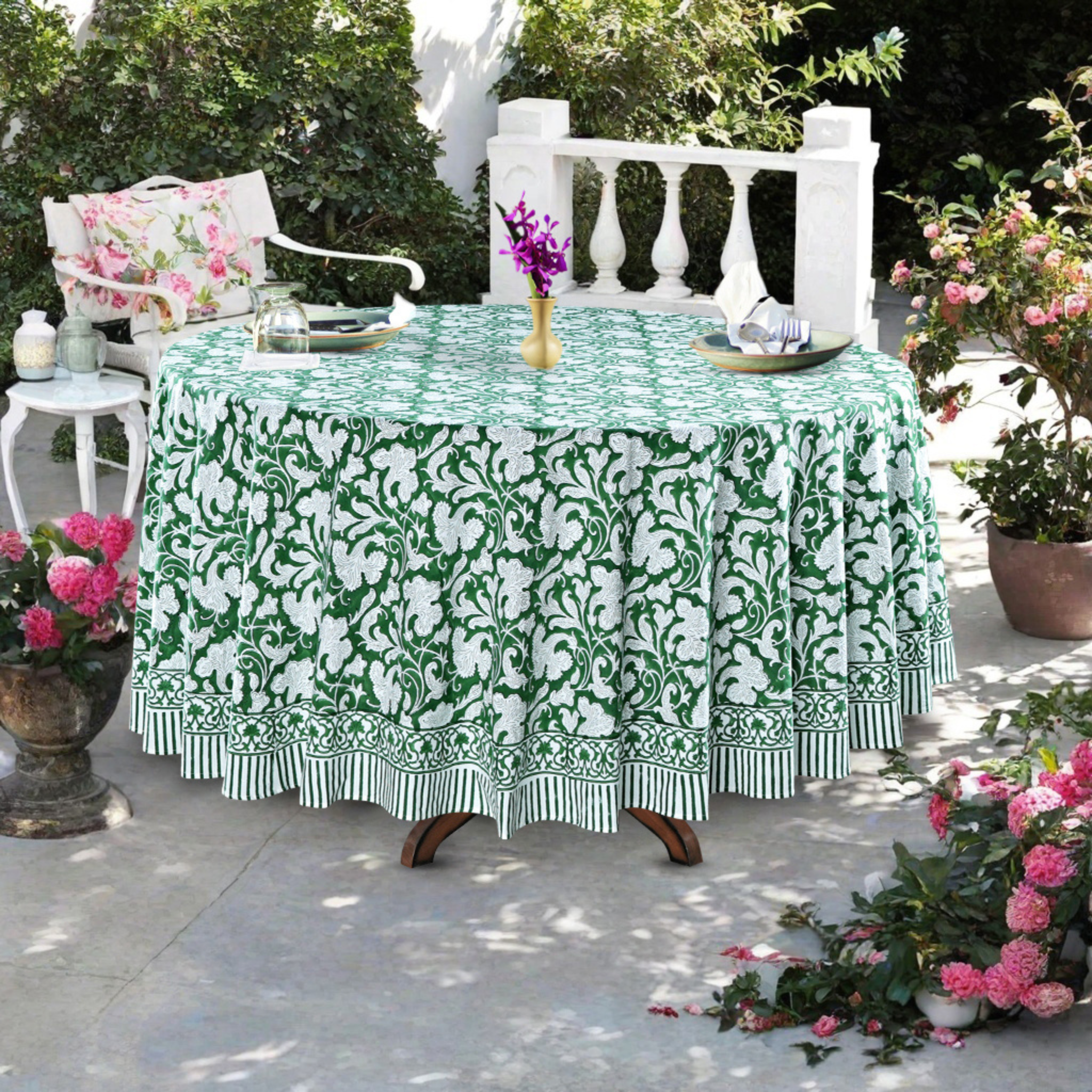 Table with a green and white floral tablecloth outdoors, surrounded by potted plants.