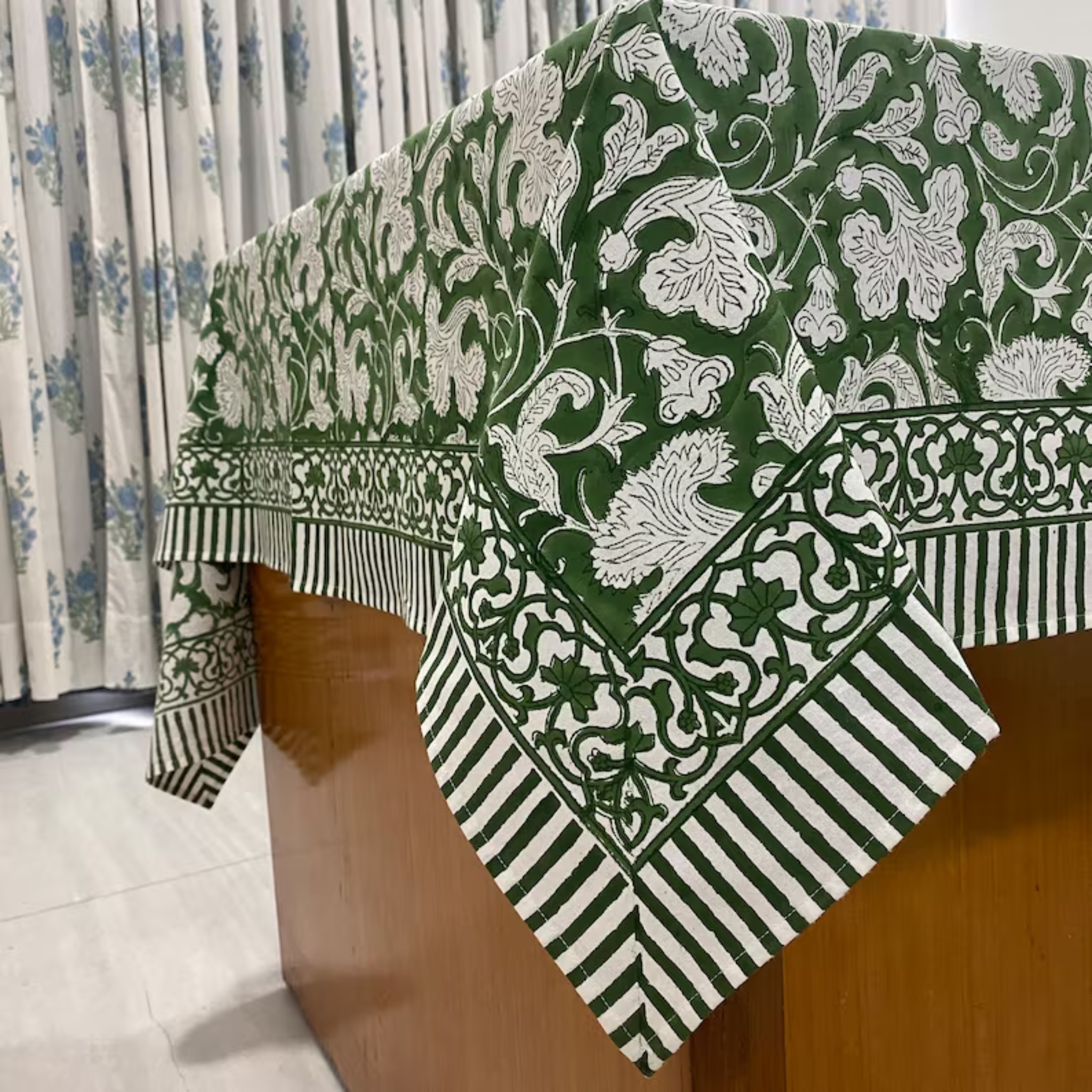 Green and white patterned tablecloth on a wooden table with floral curtains in the background