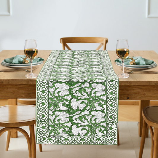 Green and white patterned table runner on a wooden table with wine glasses and plates.