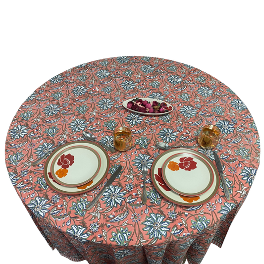 Round table with floral patterned tablecloth, plates, and glasses on a white background