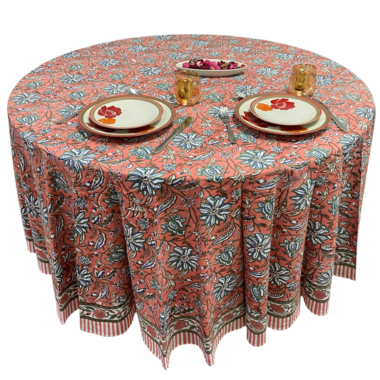 Round table with a floral patterned tablecloth, plates, and cutlery on a white background