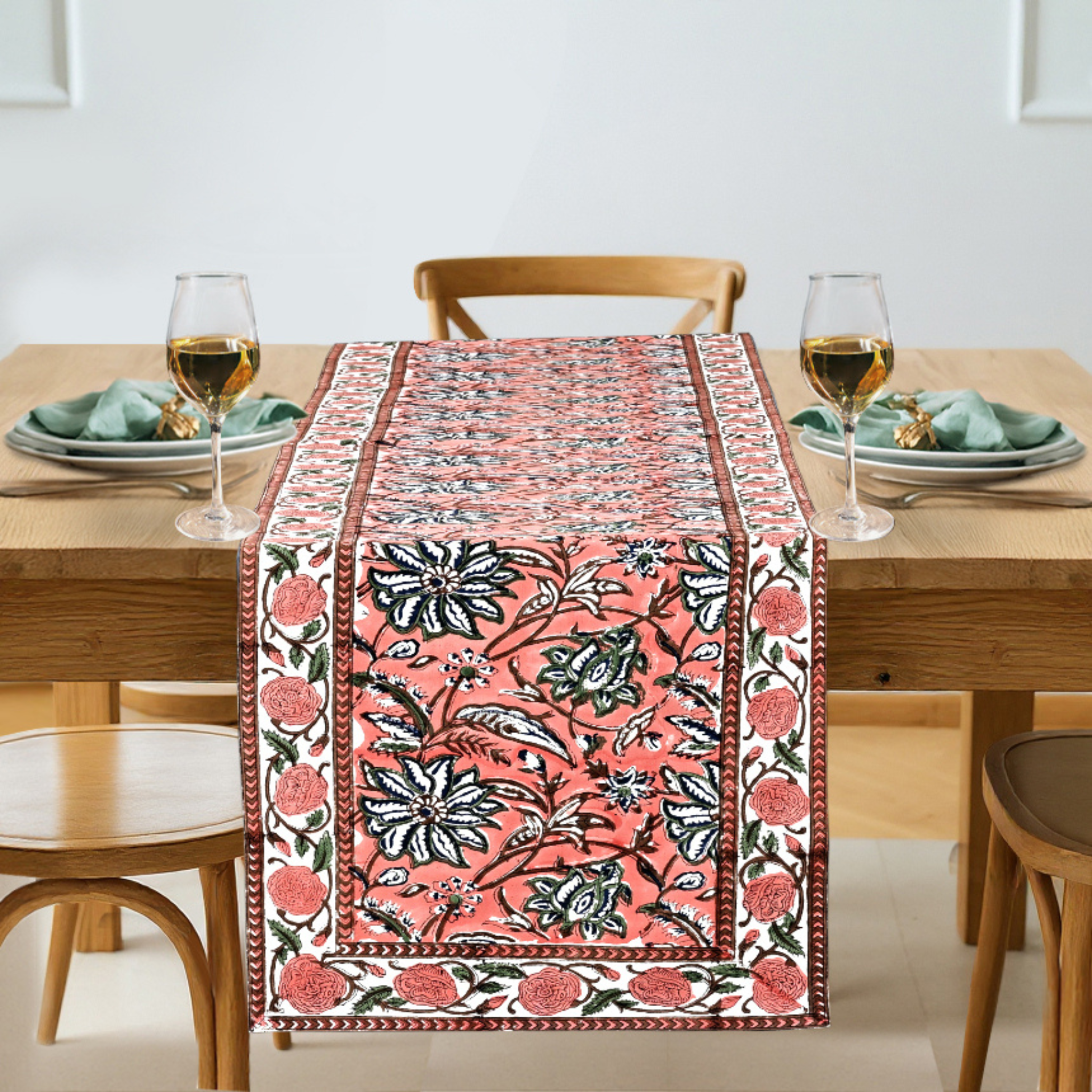 Dining table with a floral patterned table runner, glasses, and plates.
