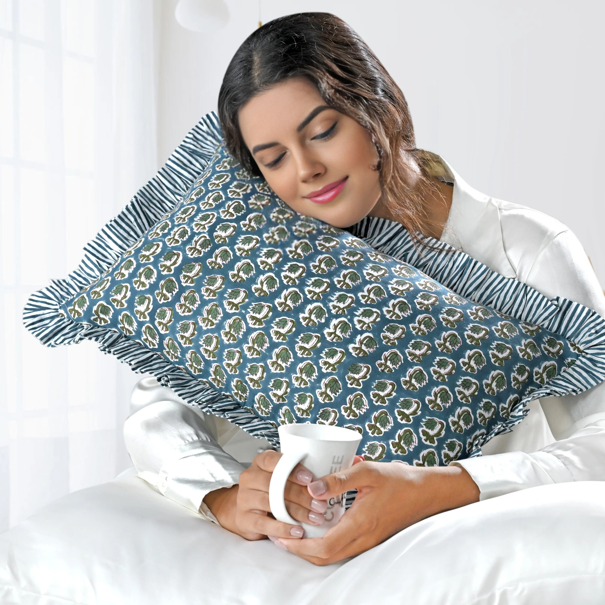Woman holding a patterned pillow and a mug in bed