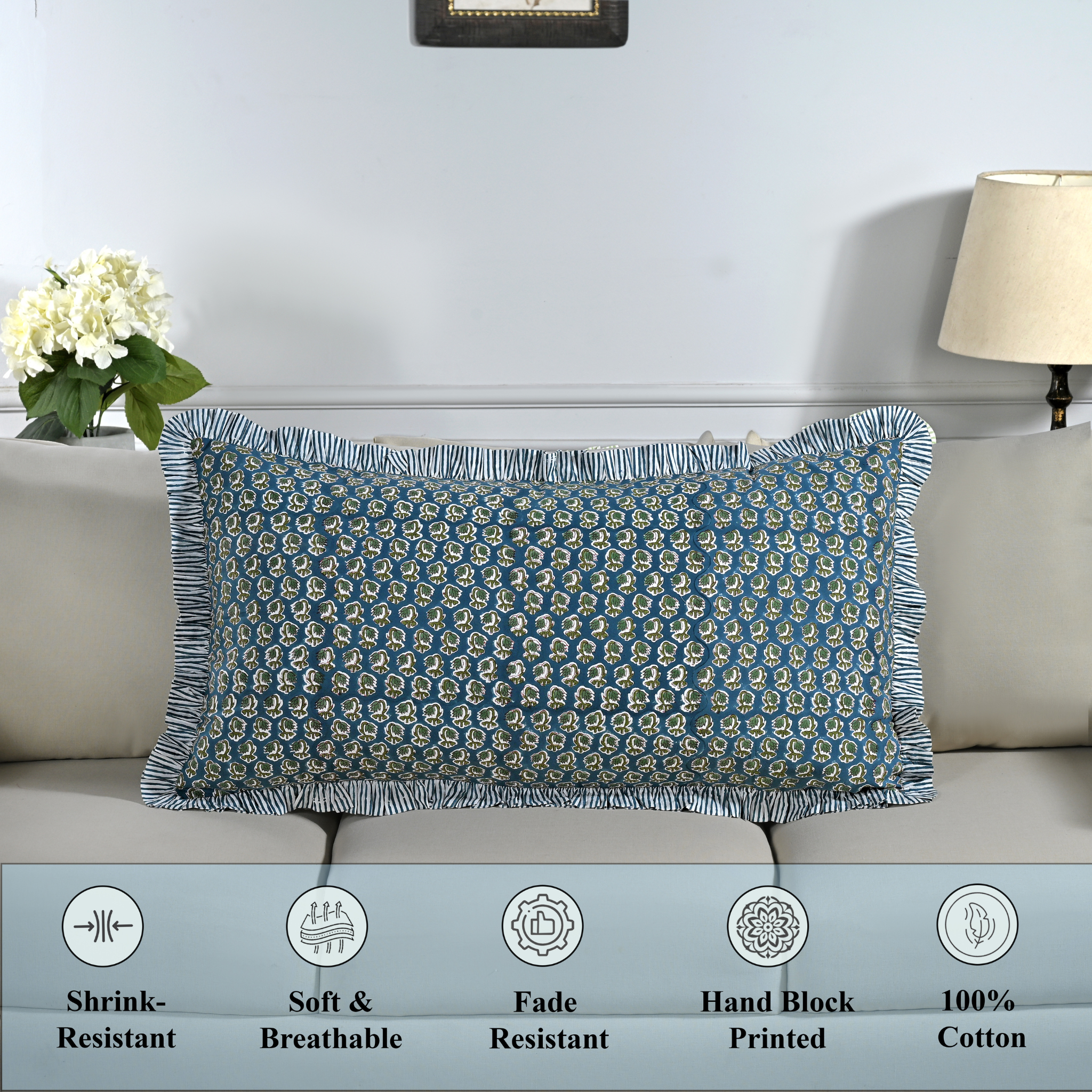 Cotton block print pillow cover placed on a bed with lamp and flowers in background.