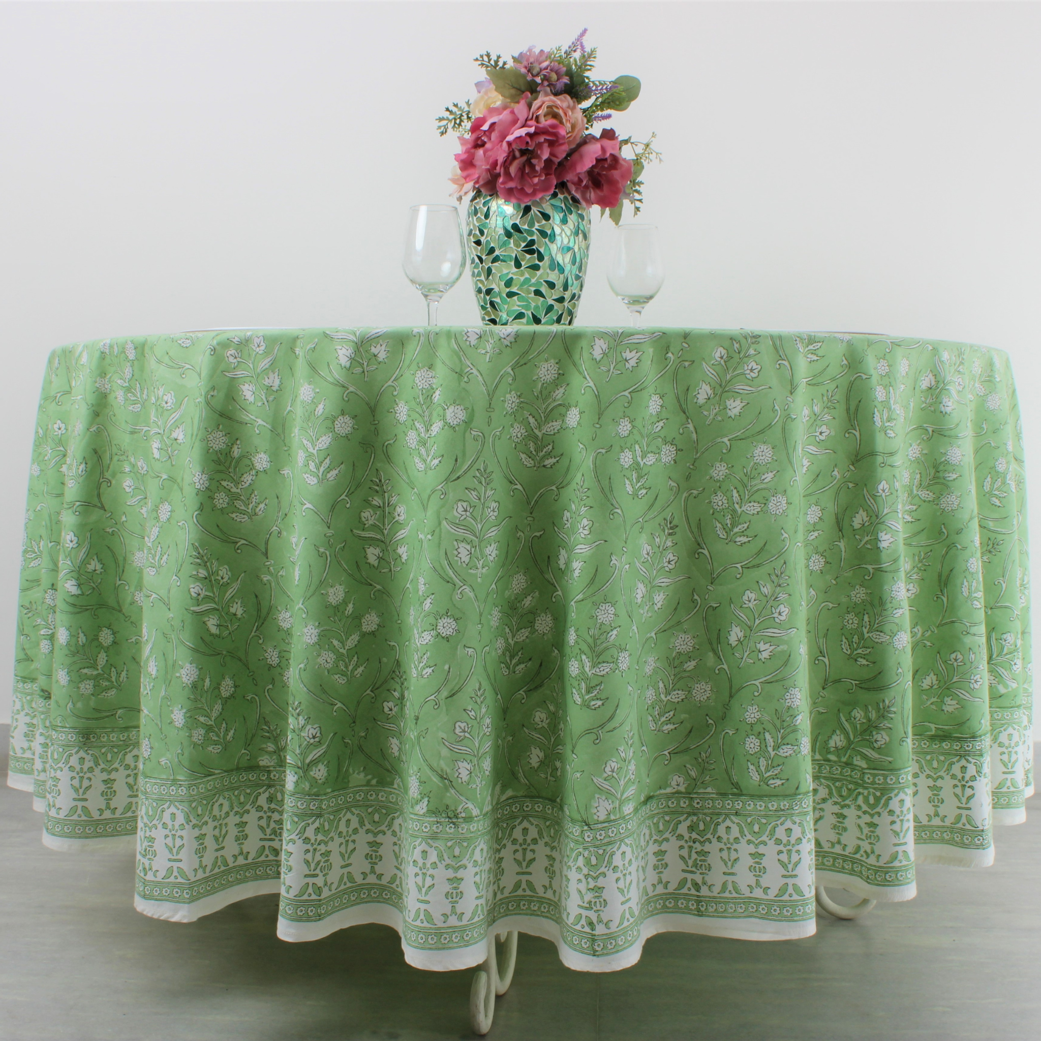 Green patterned tablecloth on a table with a vase of flowers and wine glasses.