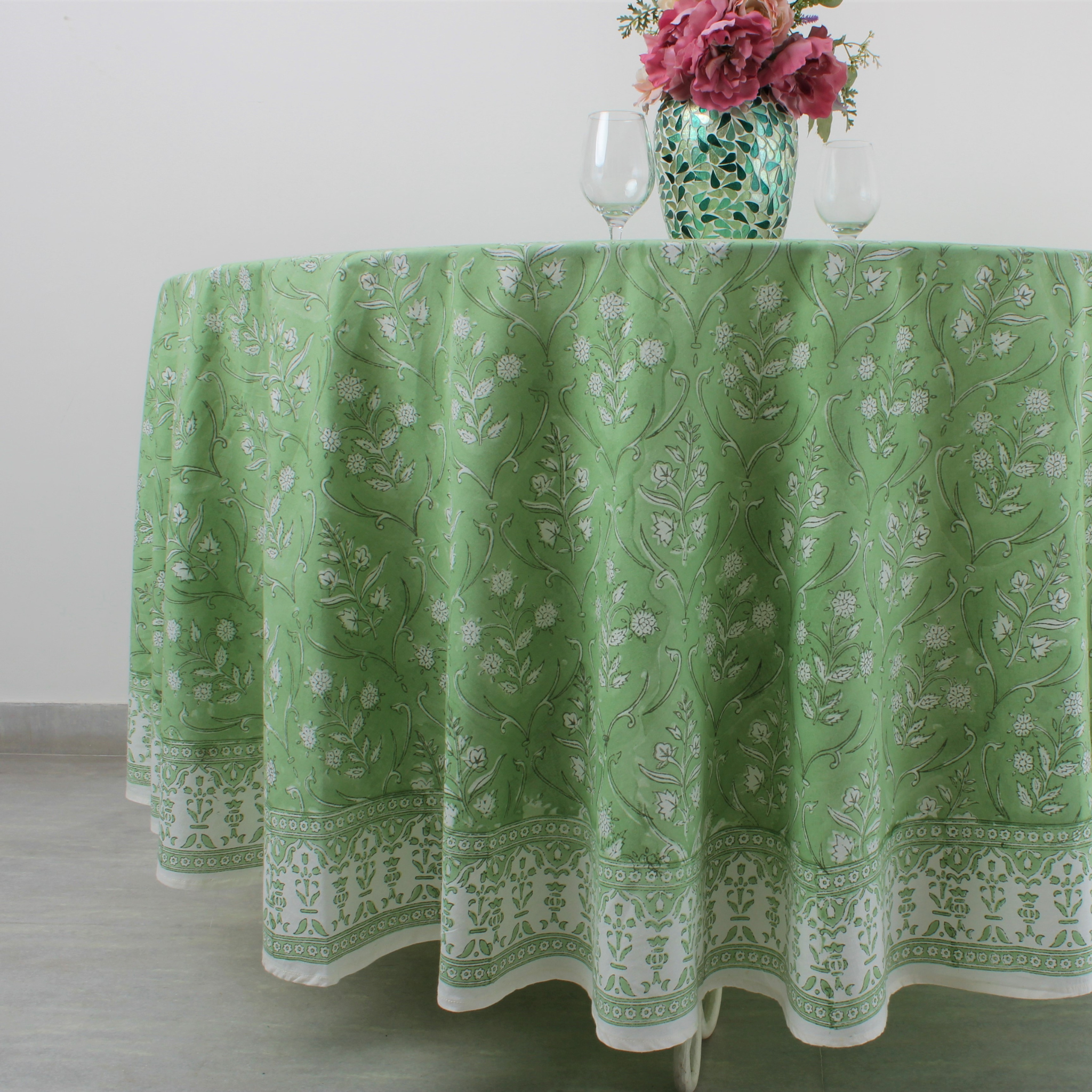 Green patterned tablecloth on a round table with a vase of flowers.