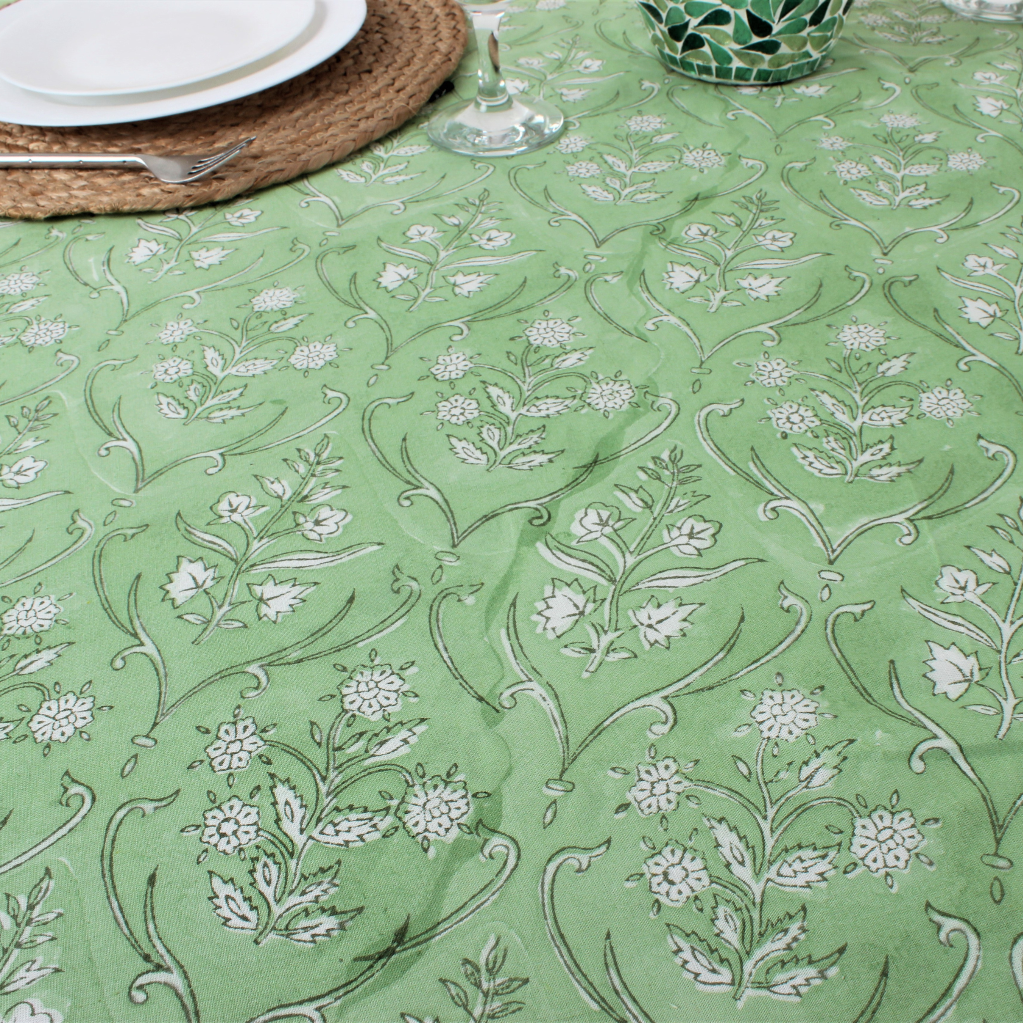 Green tablecloth with white floral pattern on a table setting.