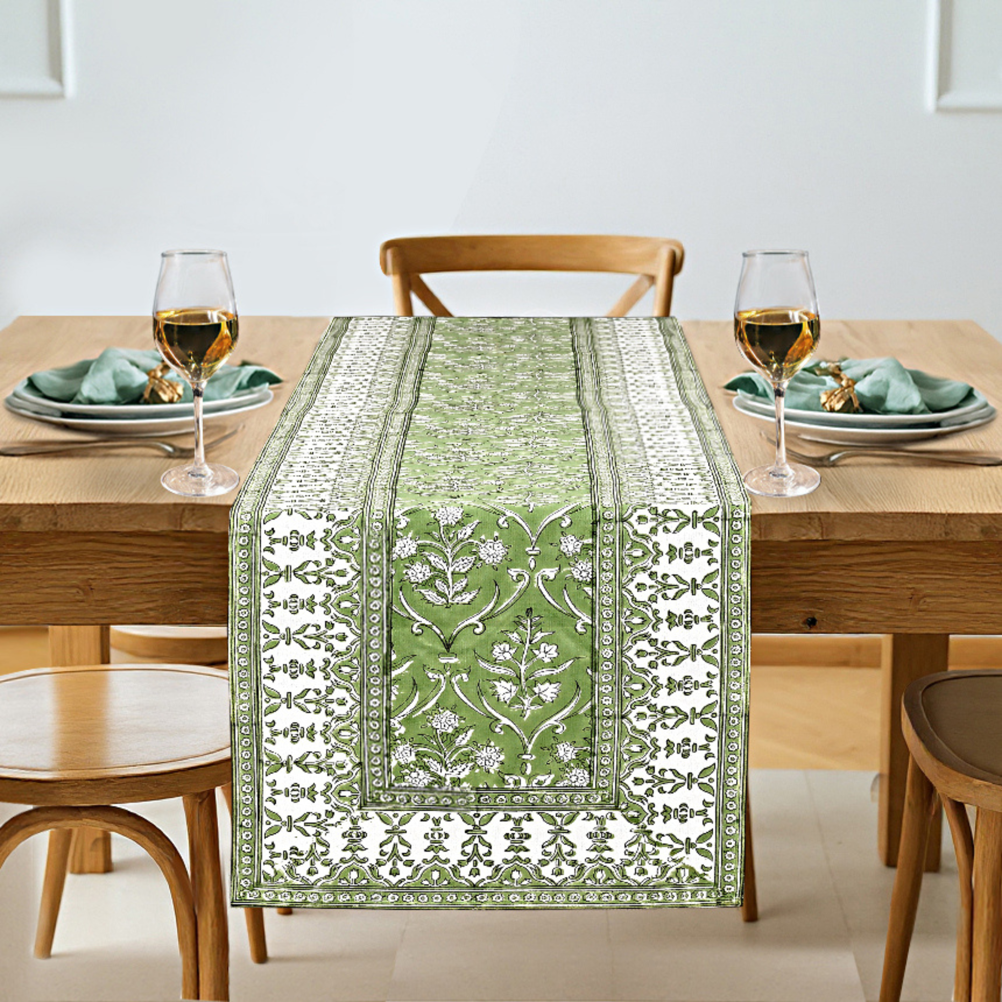 Dining table with a green and white patterned table runner, glasses, and plates.