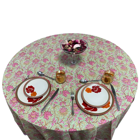 Round table with floral tablecloth set for a meal, including plates, cutlery, and glasses.