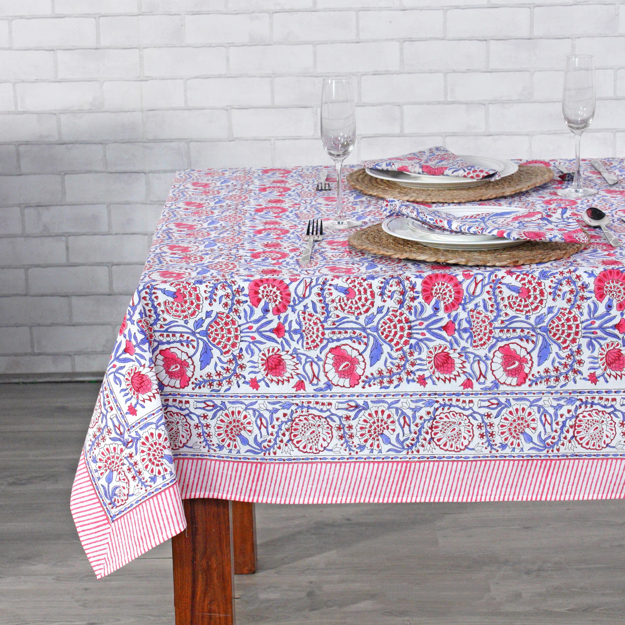 Tablecloth with floral pattern on a wooden table against a white brick wall.