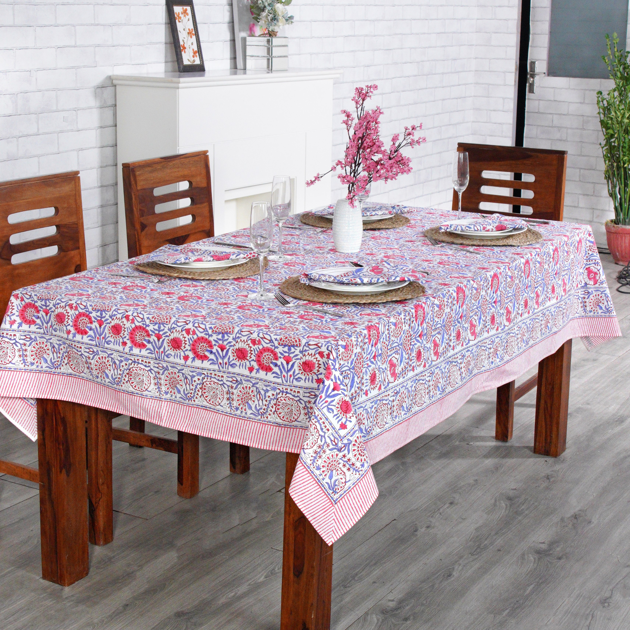 Dining table with a floral tablecloth, wooden chairs, and decorative items.