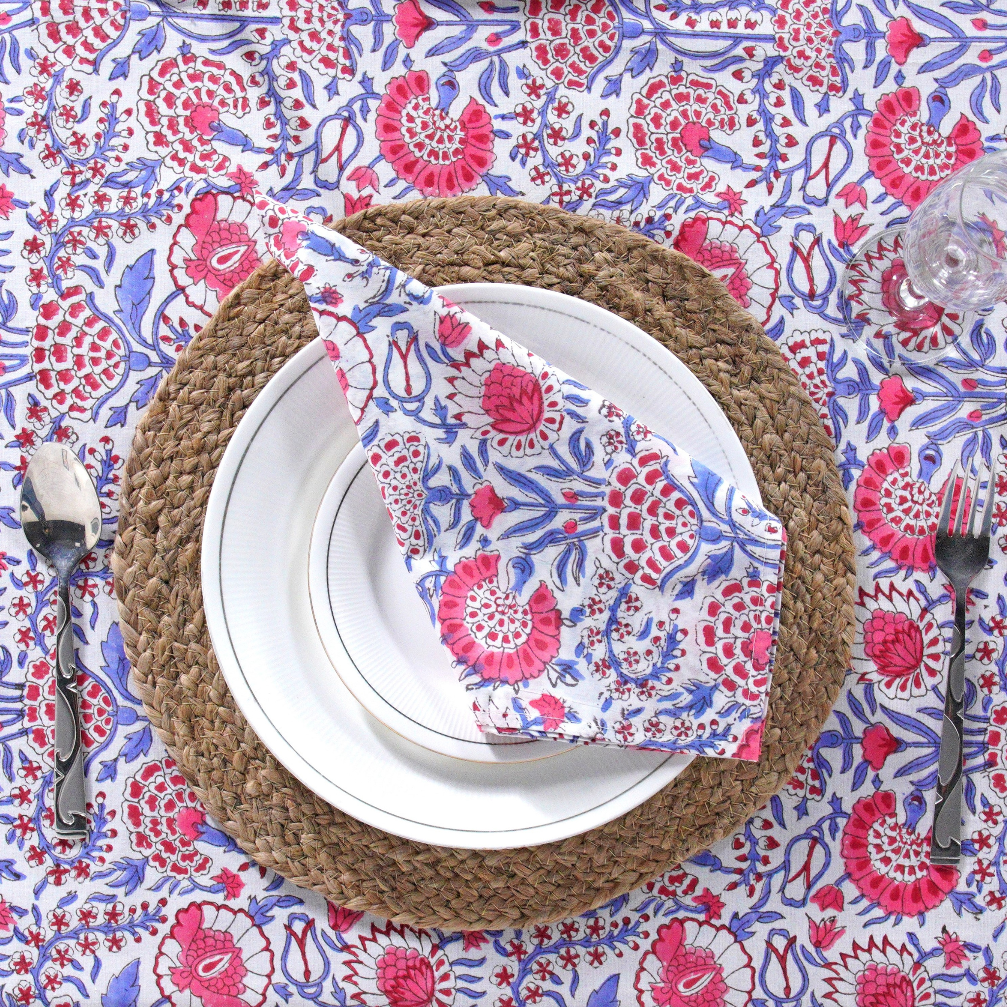 Placemat with white plate, folded floral napkin, and cutlery on a patterned tablecloth.