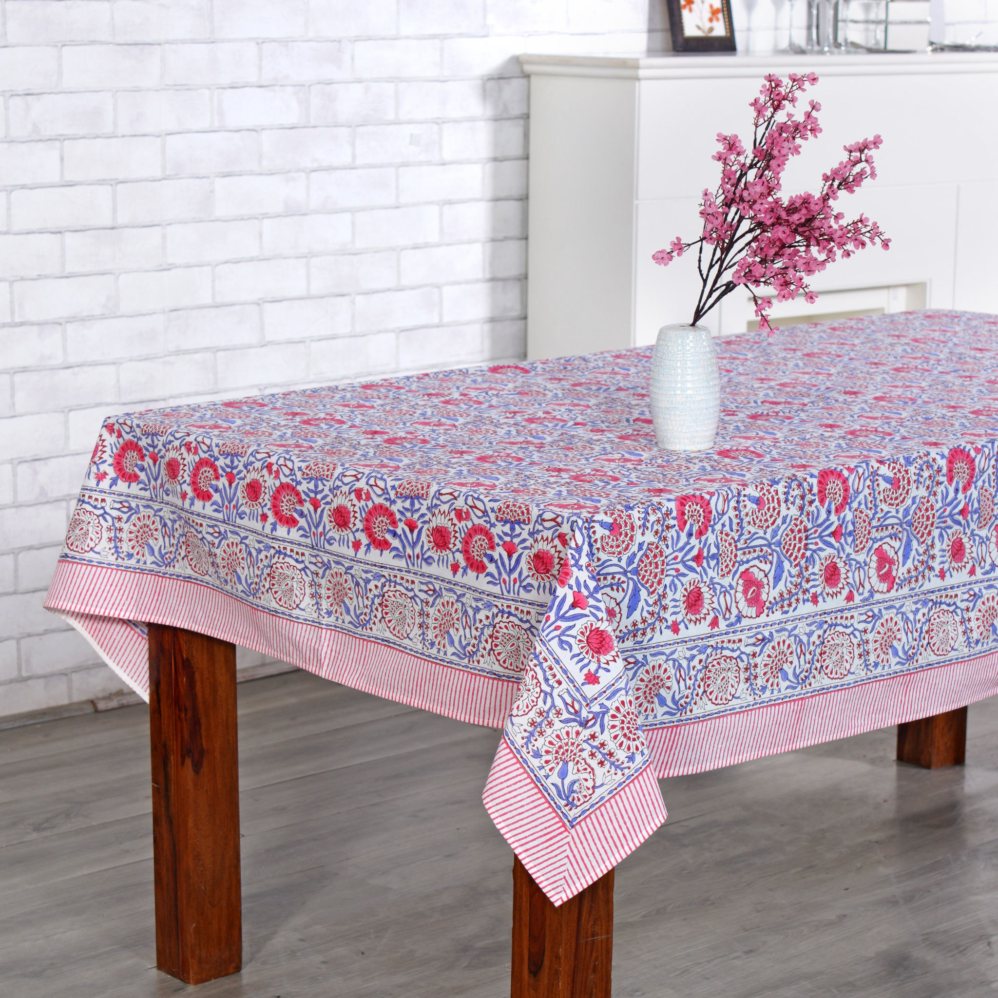 Tablecloth with floral pattern on a wooden table against a white brick wall.