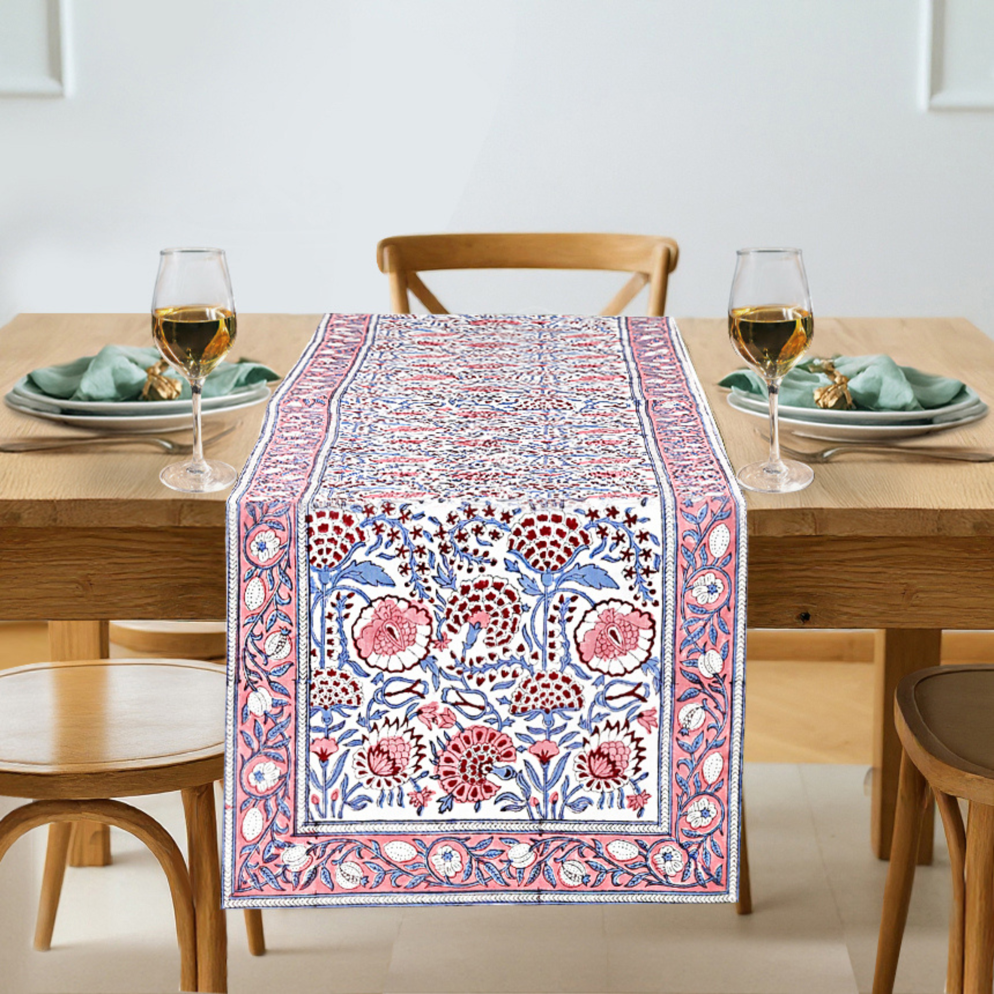 Dining table with a patterned table runner, glasses, and plates.