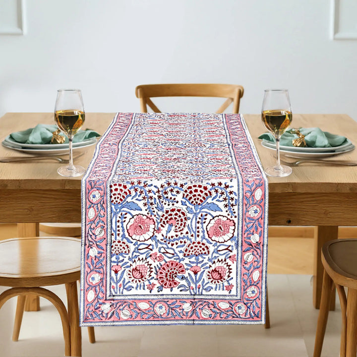 Dining table with a patterned table runner, glasses, and plates.