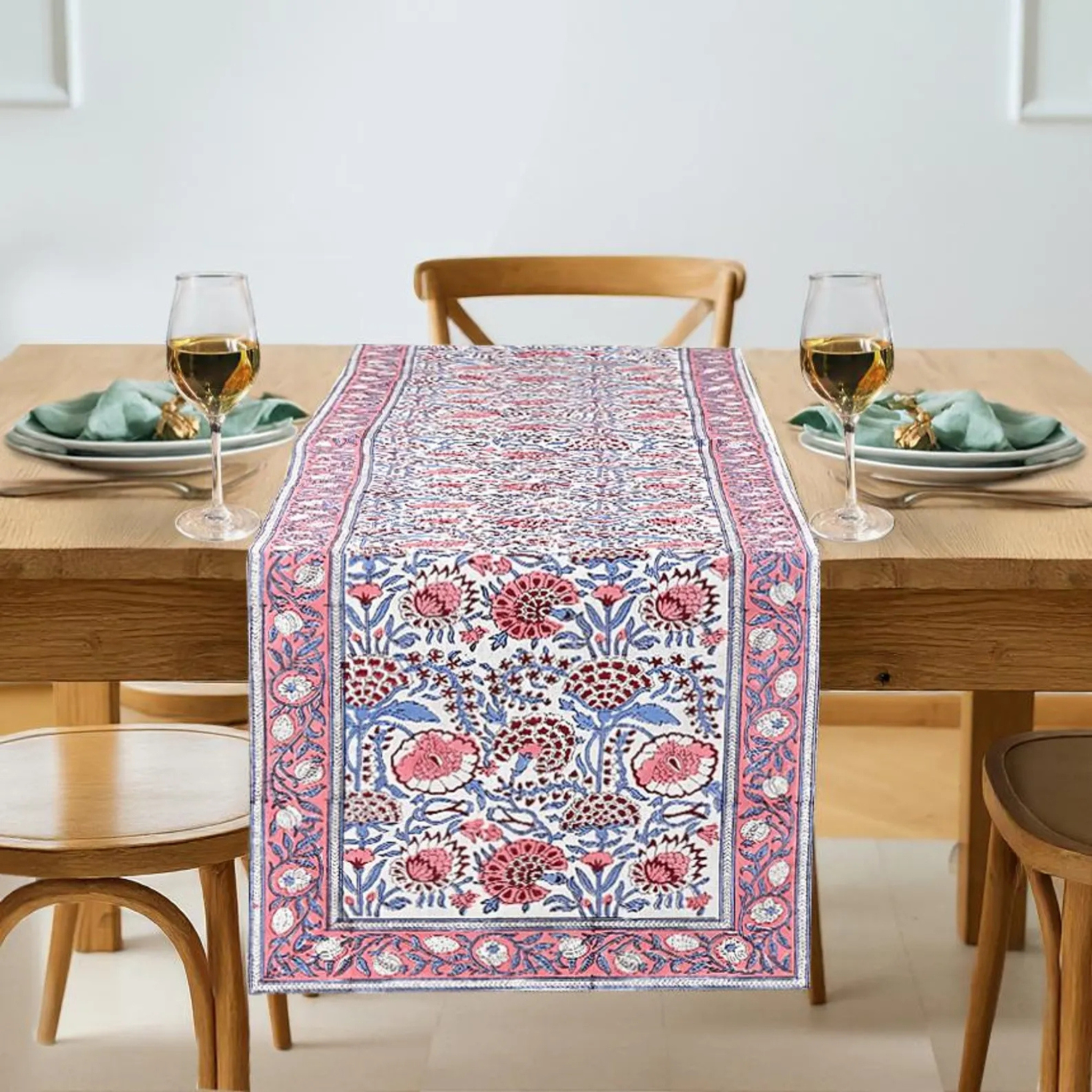 Dining table with a floral patterned table runner, glasses, and plates.