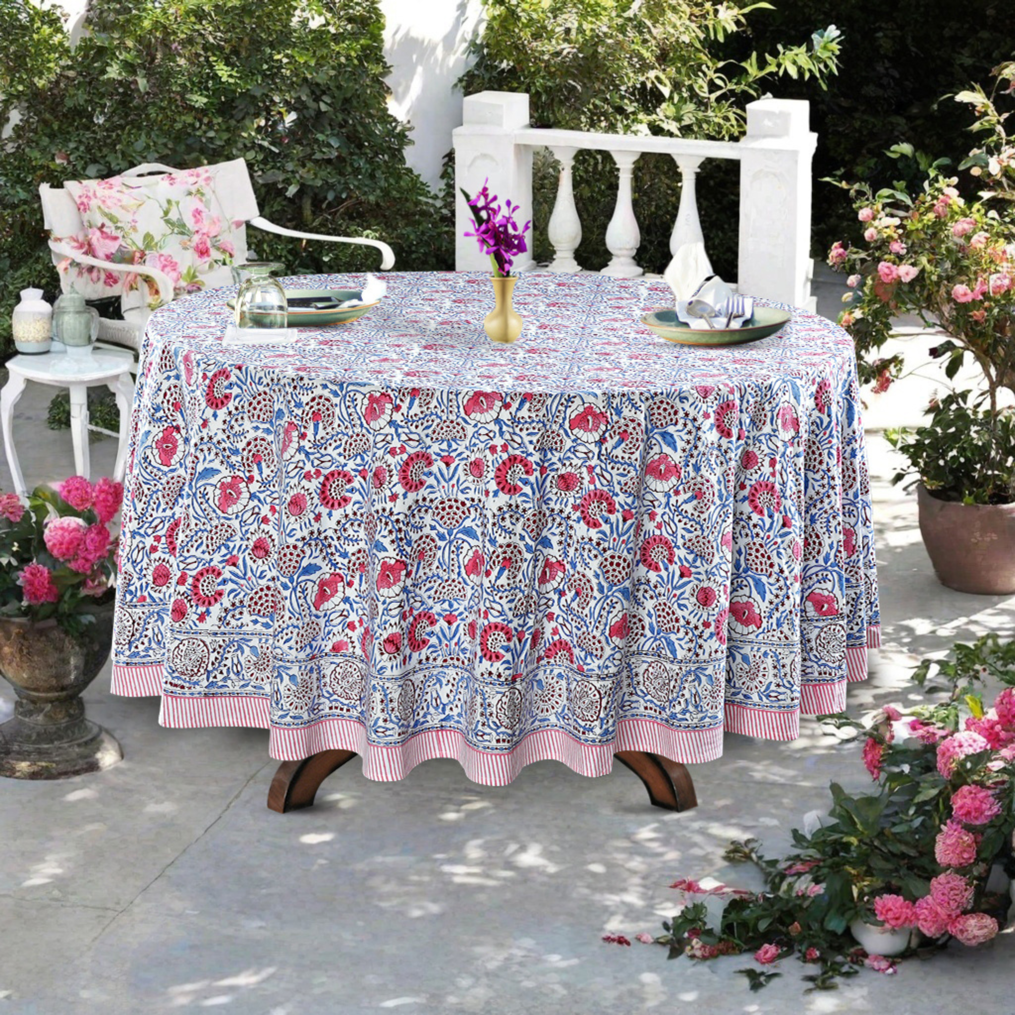 Floral patterned tablecloth on a table outdoors with chairs and flowers.