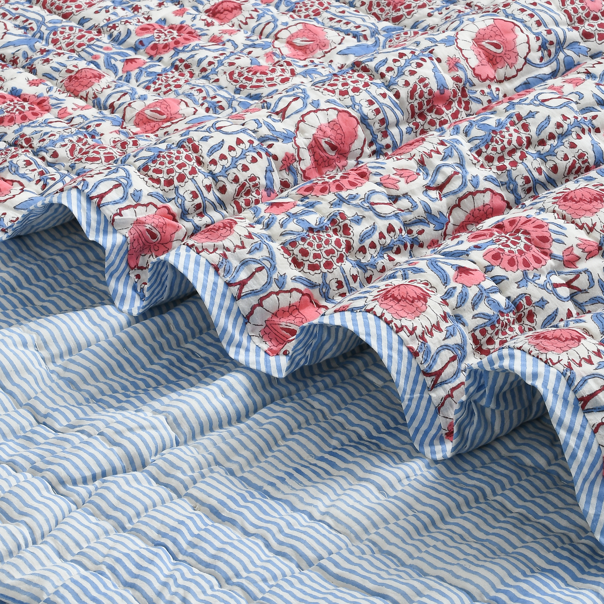 Floral quilt with red and white pattern on a blue striped bedspread