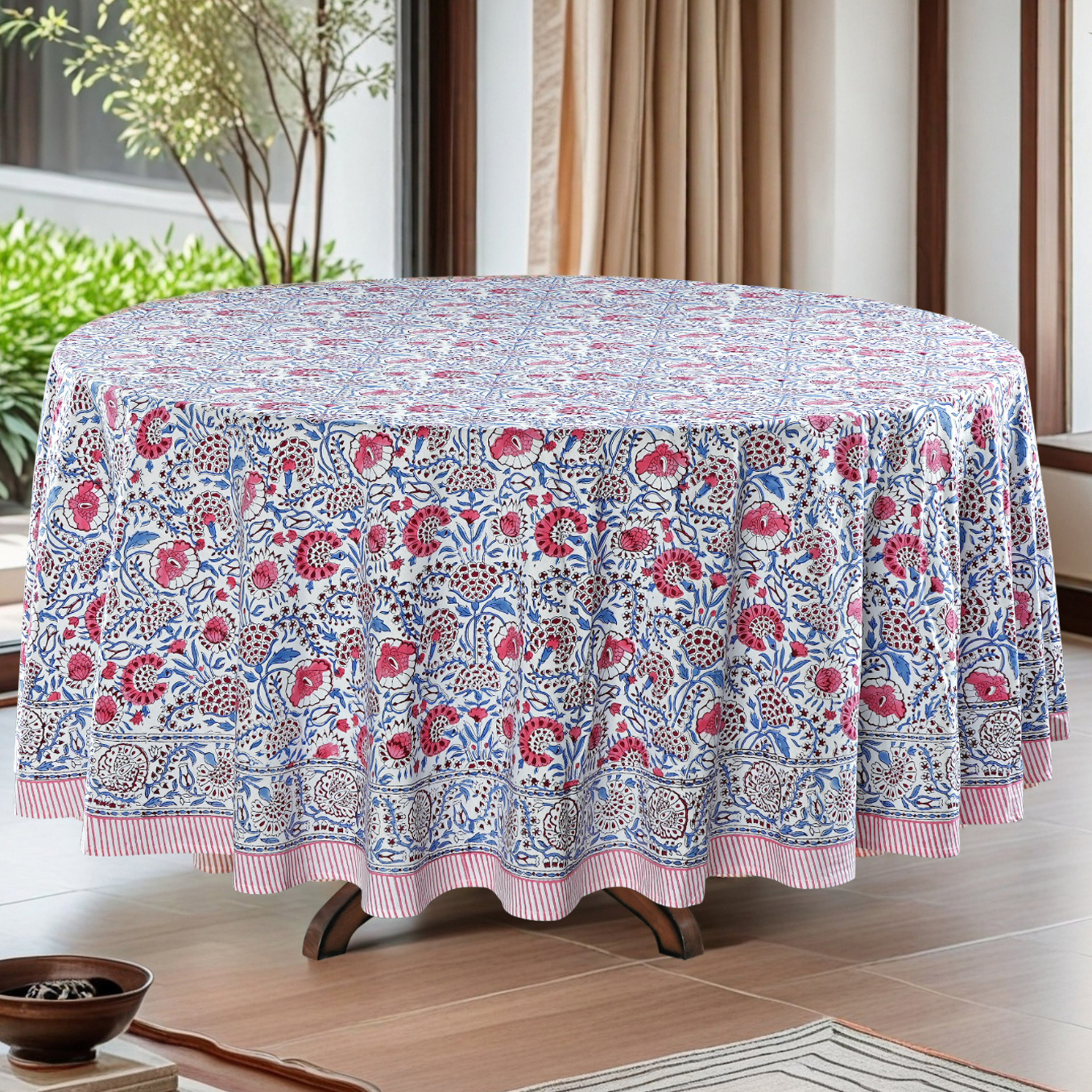 Round tablecloth with floral pattern in a room with a window and plant.