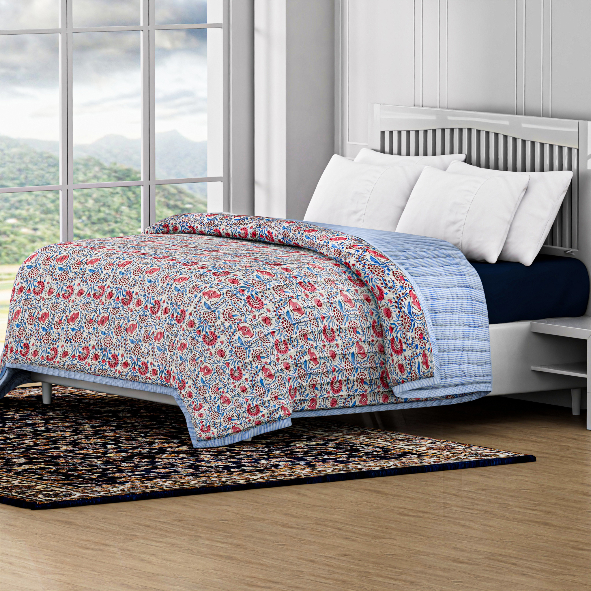 Floral quilt on a bed in a room with large windows and a view of greenery outside.
