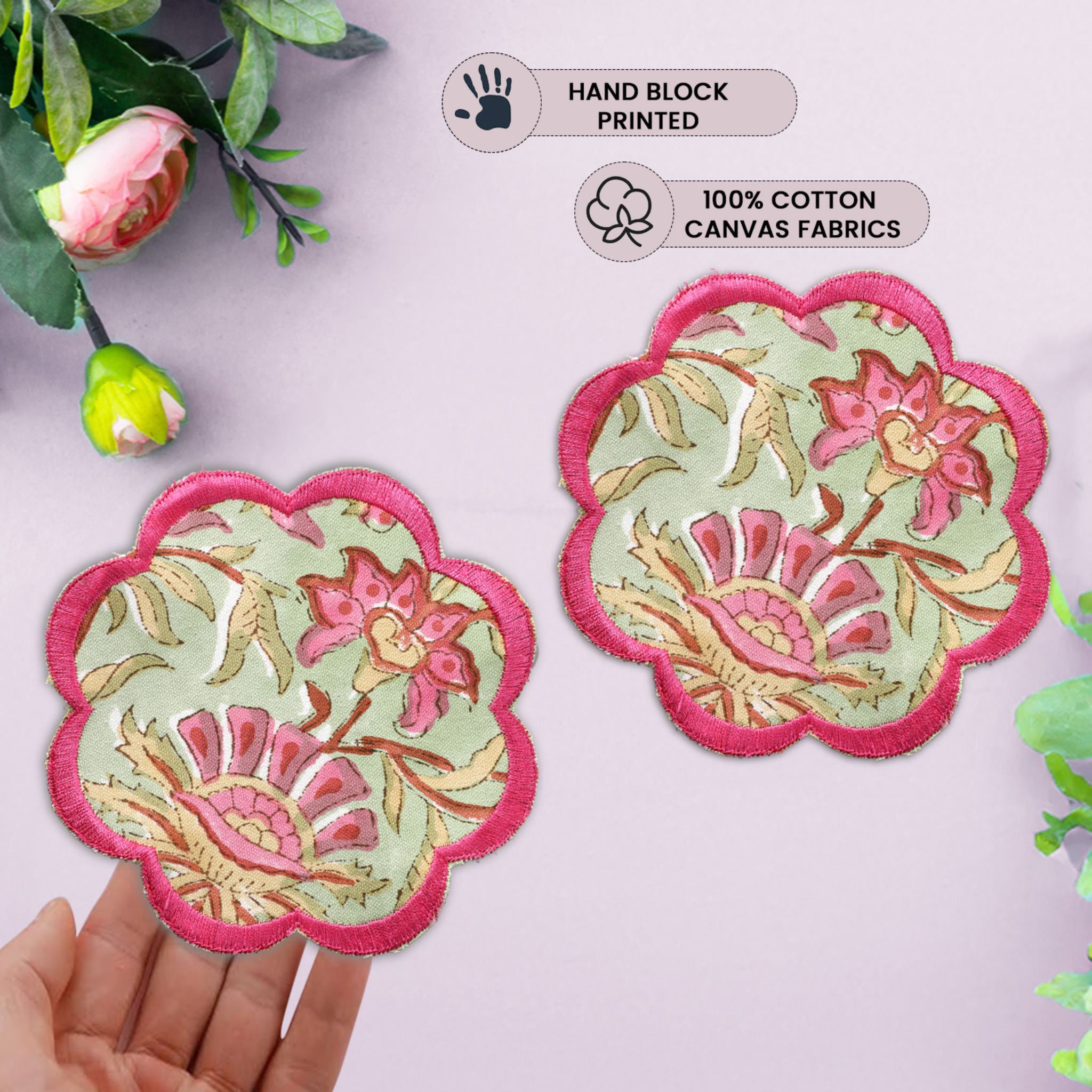 Two floral fabric coasters with pink edges on a light purple background, held by a hand.