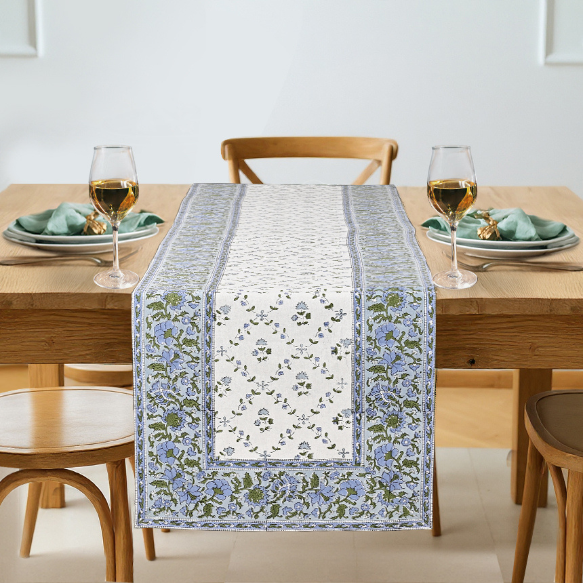 Dining table with a floral table runner, glasses, and plates on a light background