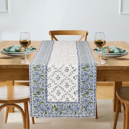 Dining table with a floral table runner, glasses, and plates on a light background