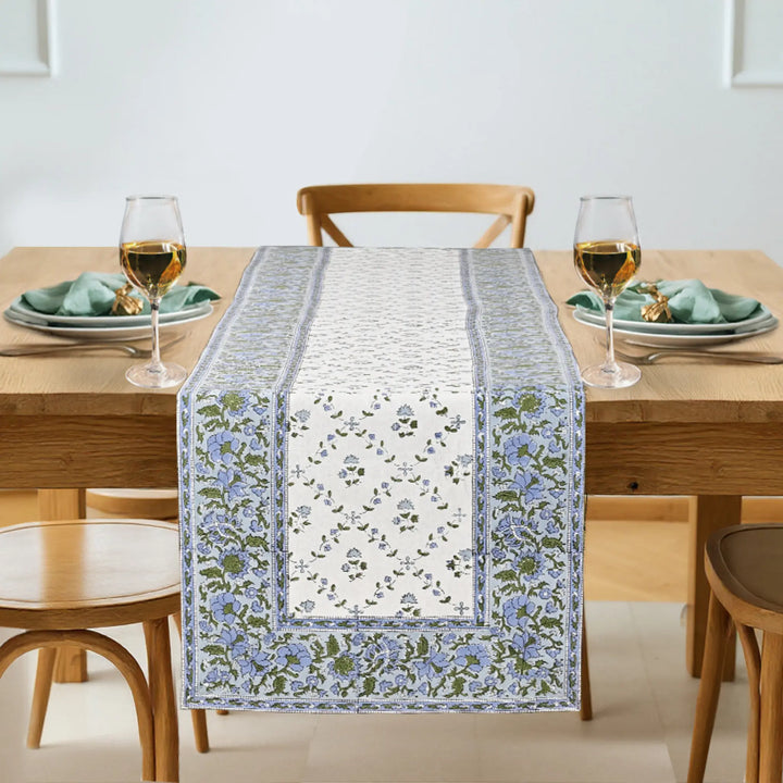 Dining table with a floral table runner, glasses, and plates on a light background