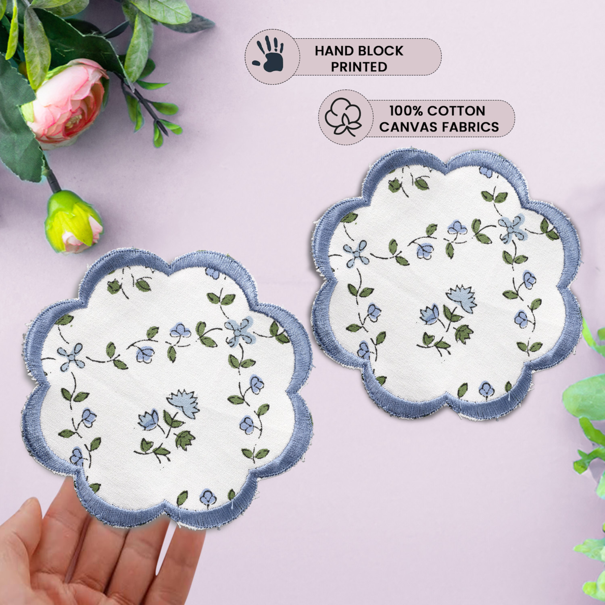 Two floral coasters with scalloped edges on a light pink background, held by a hand.