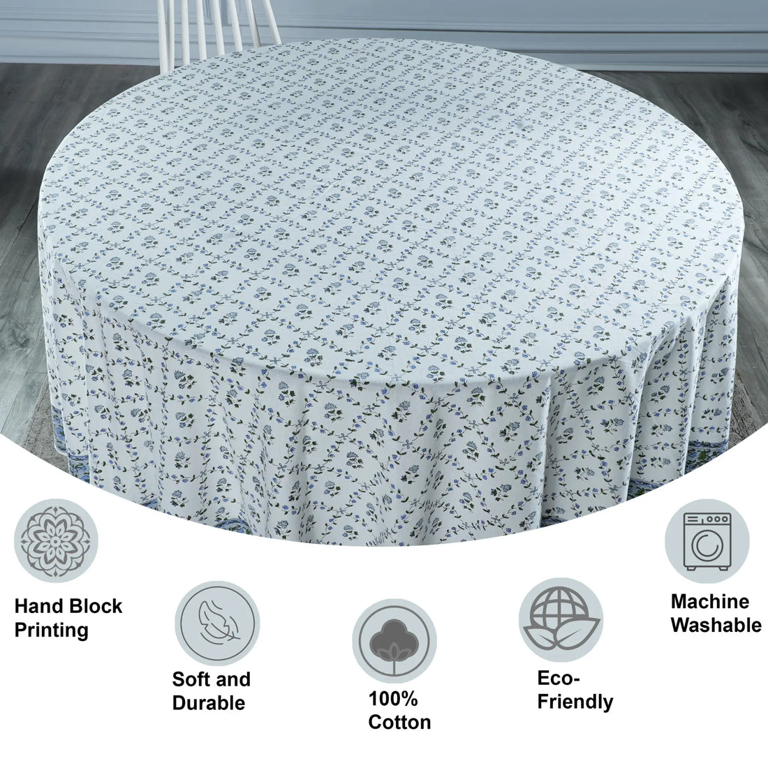 Round table covered with a floral patterned tablecloth on a wooden floor.