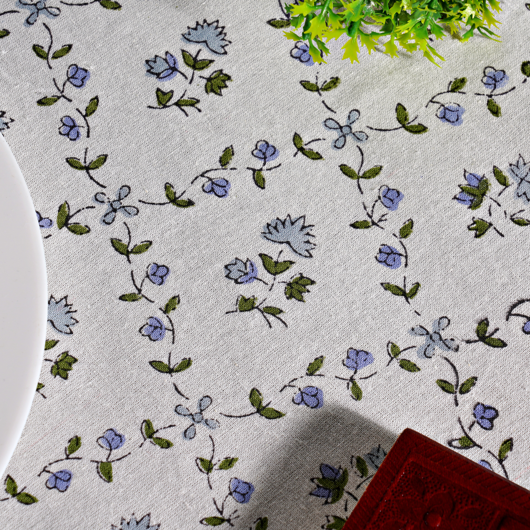 Floral patterned tablecloth with blue flowers and green leaves on a white background.