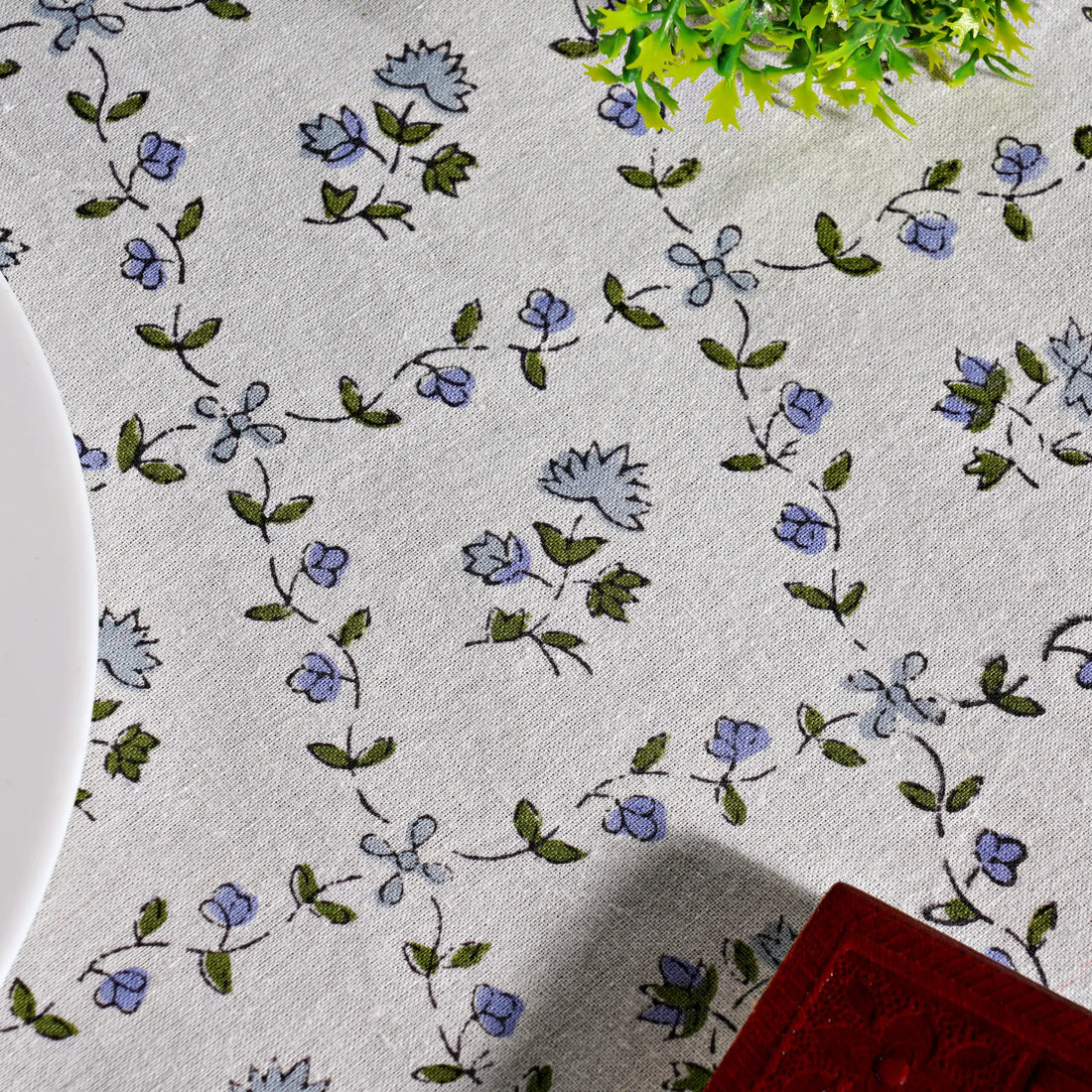 Floral patterned tablecloth with blue flowers and green leaves on a white background.