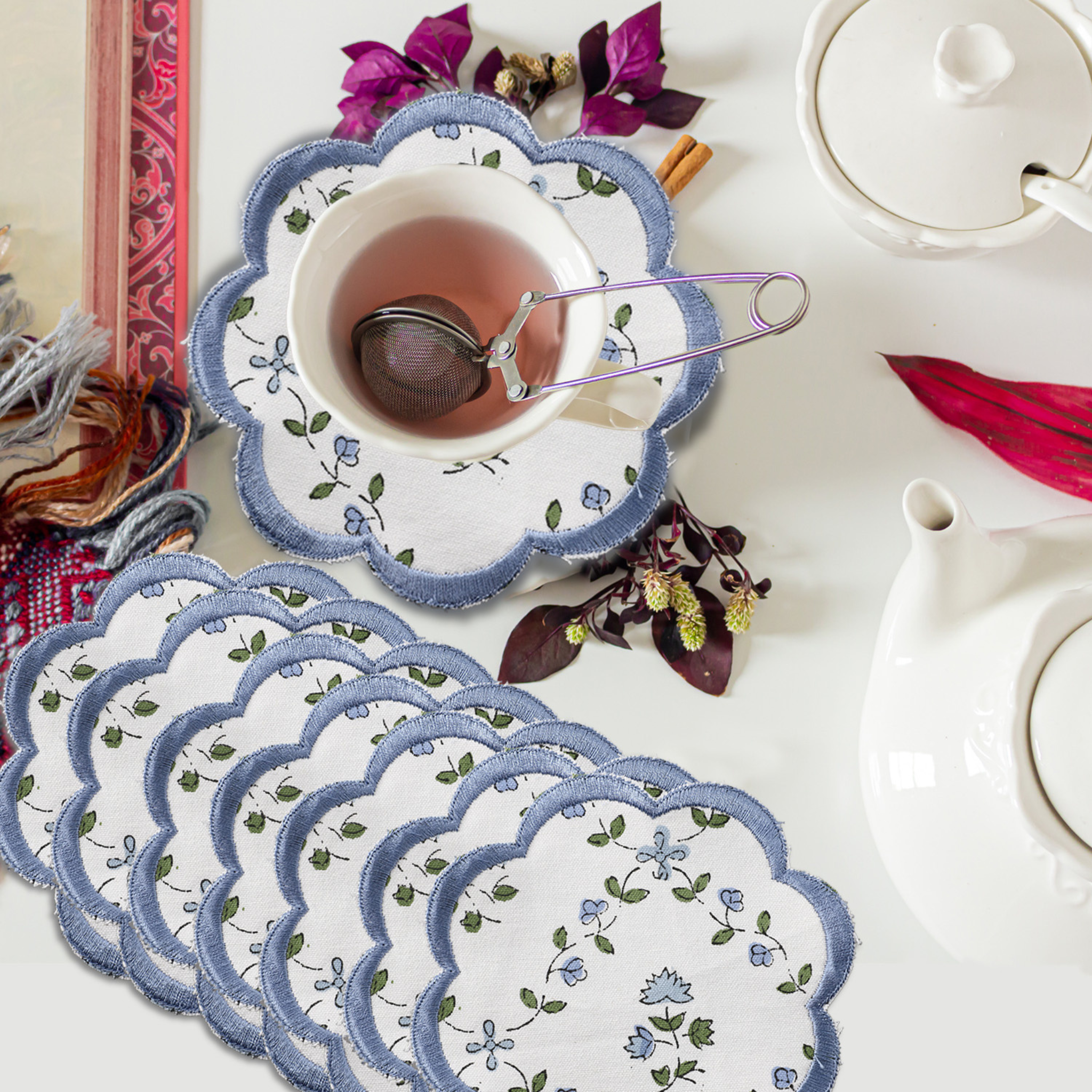 Set of floral coasters with a cup of tea and teapot on a table.