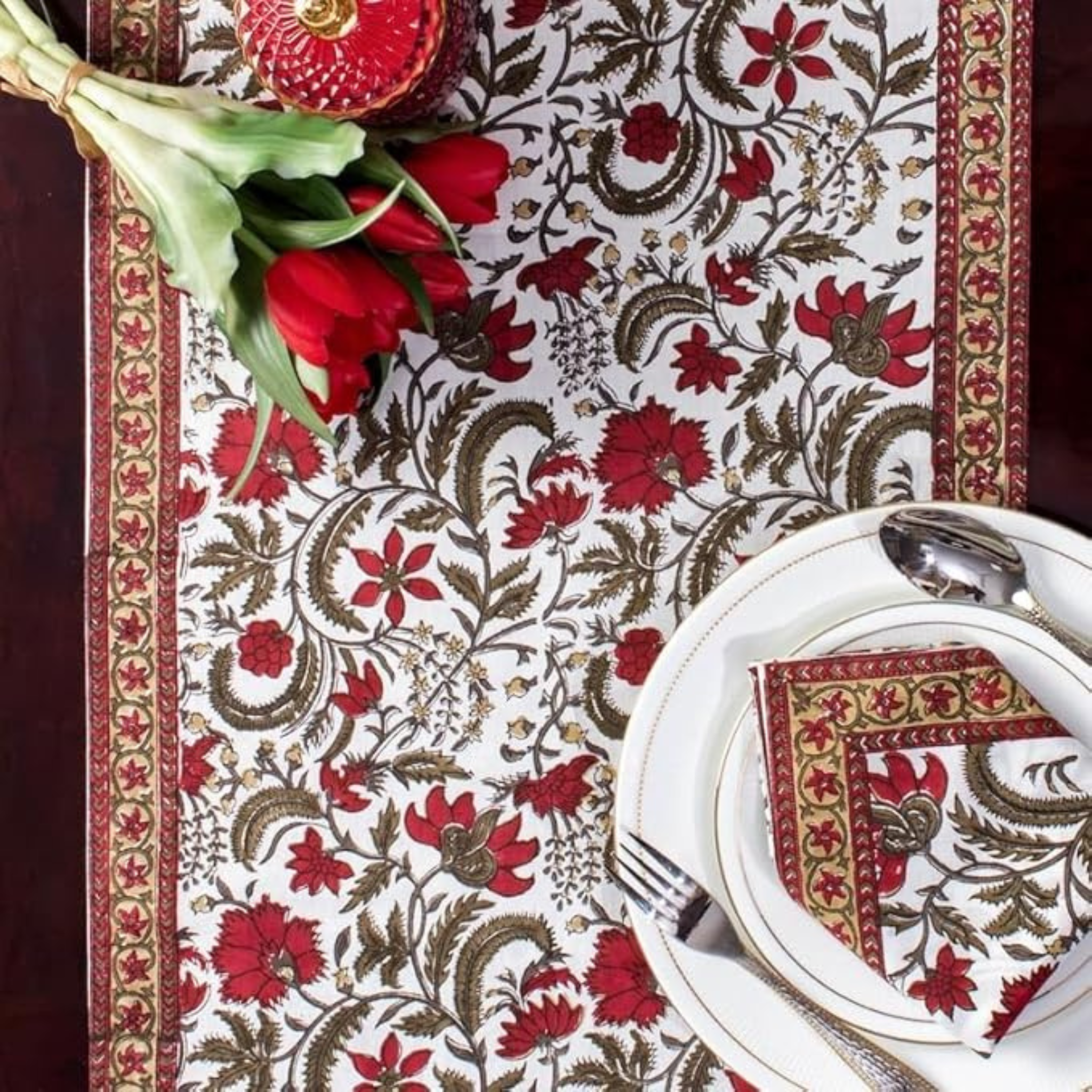 Decorative table setting with floral-patterned tablecloth, red tulips, and white plates.