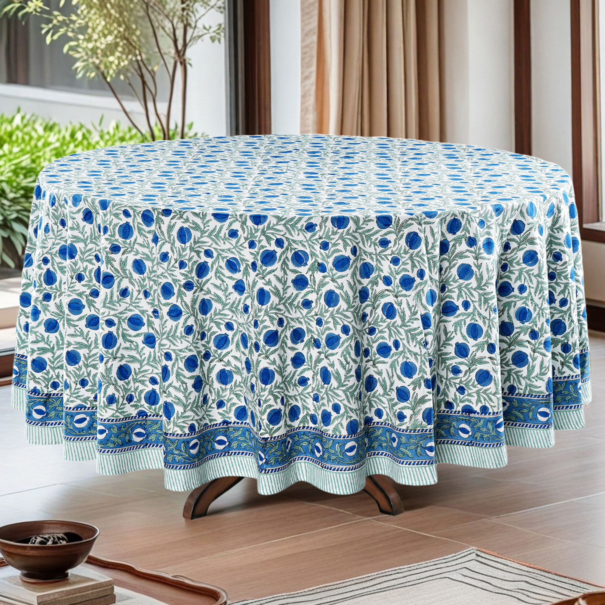 Round table with a blue and white floral patterned tablecloth in a room with plants and curtains.
