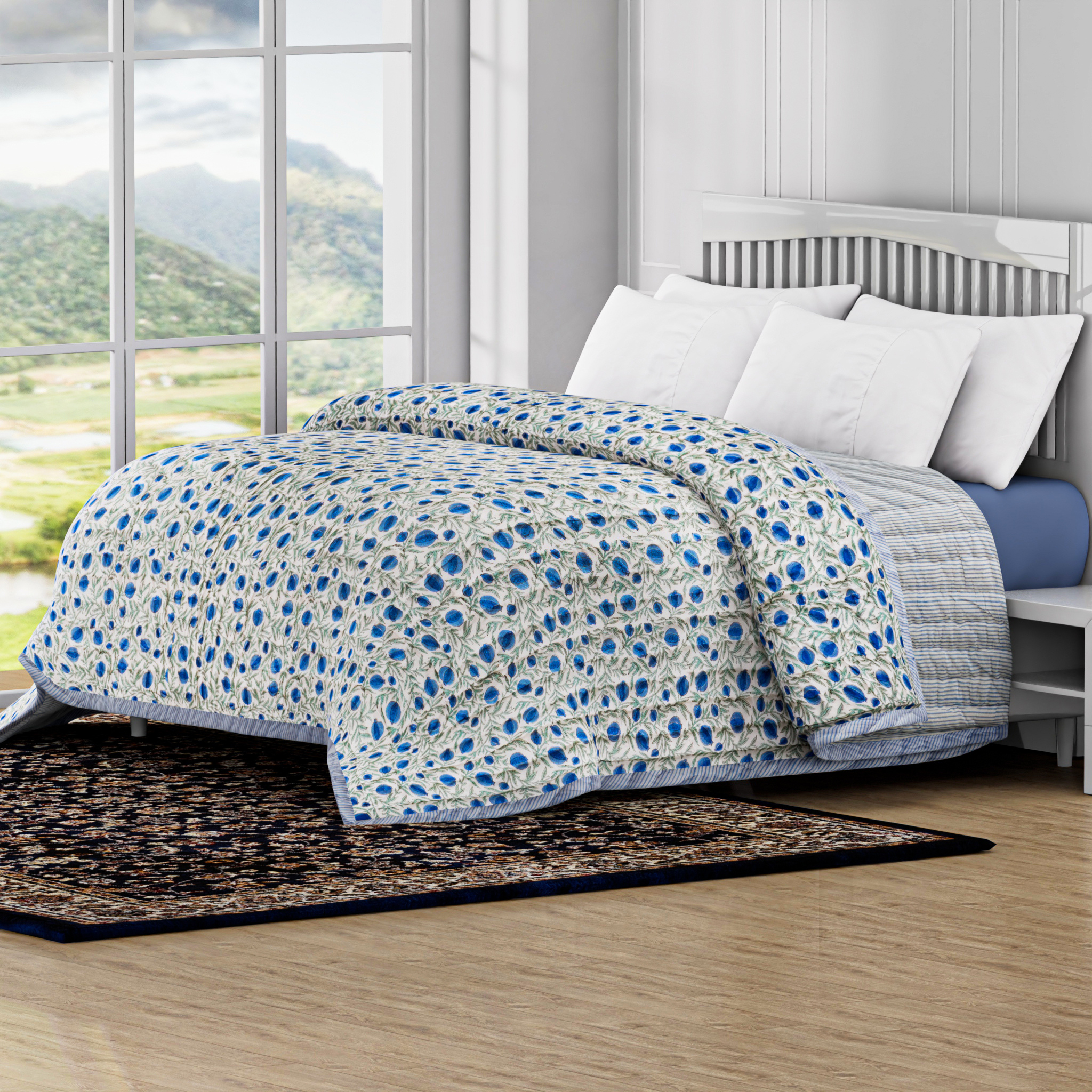 Bed with blue and white patterned comforter in a room with large windows showing a scenic view.