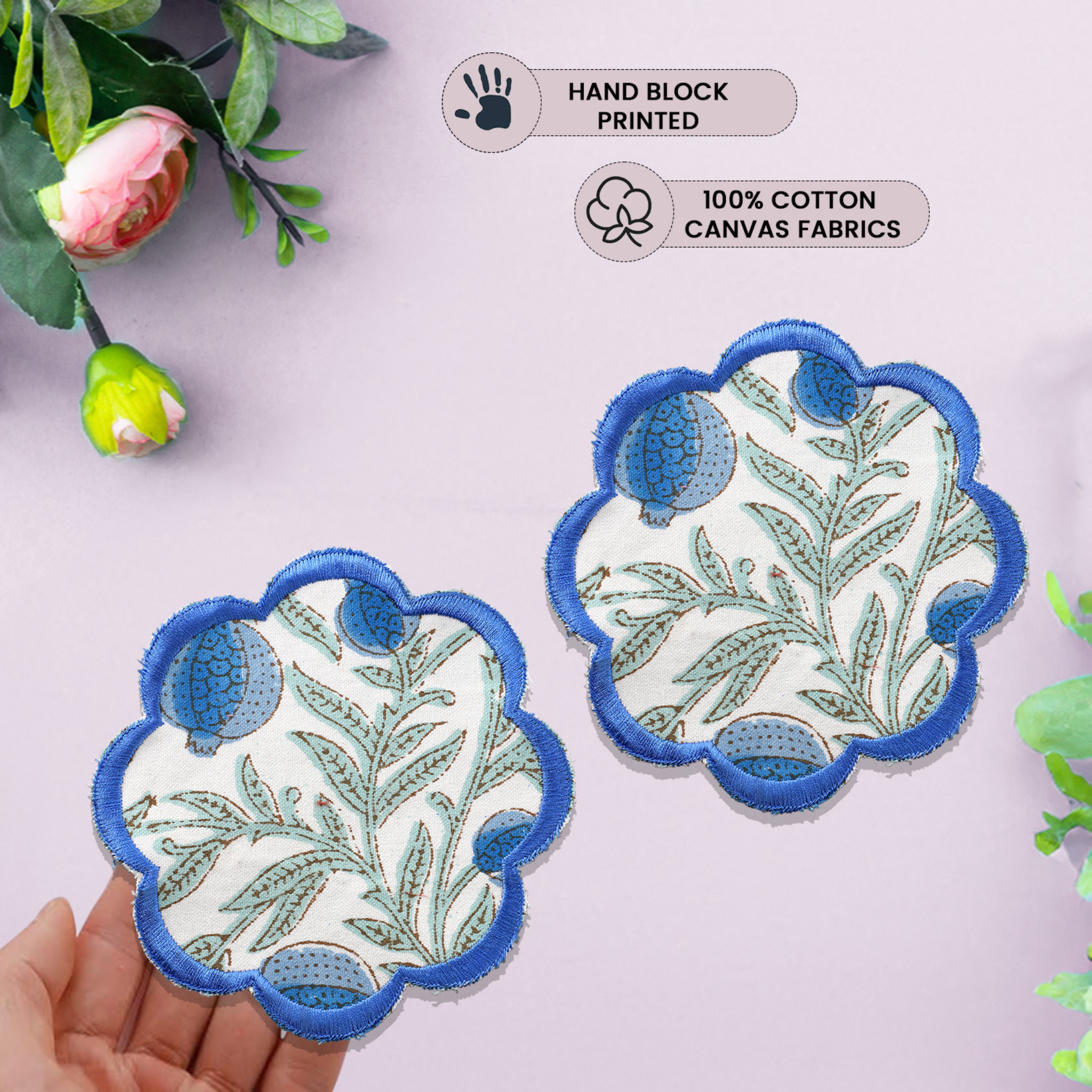 Two hand-block printed fabric patches with floral design and blue scalloped edges, held against a light pink background.
