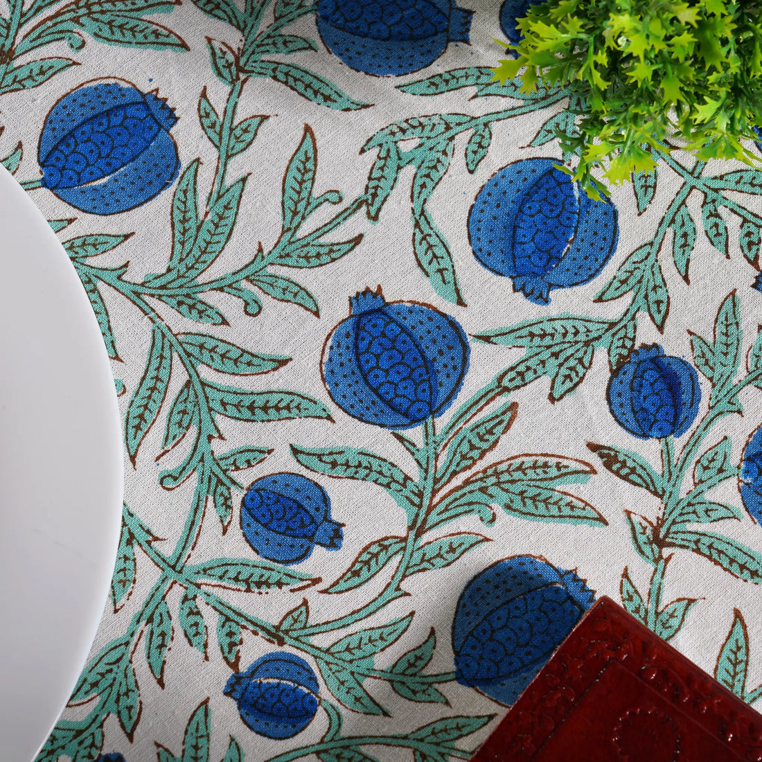 Close-up of a decorative mat with blue pomegranate and green leaf pattern.