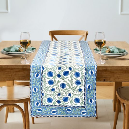 Dining table set with a decorative blue and white table runner, glasses, and plates.