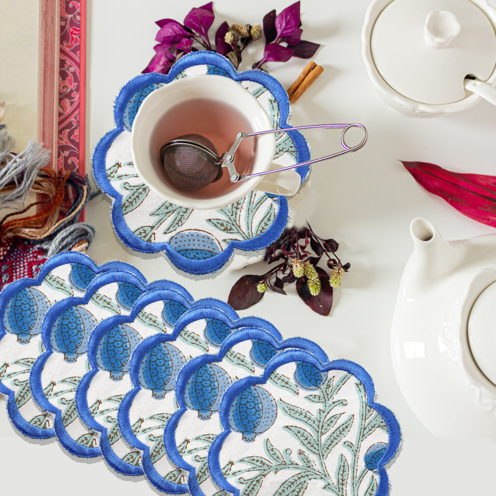 Set of embroidered coasters with blue floral patterns on a white surface with tea accessories.
