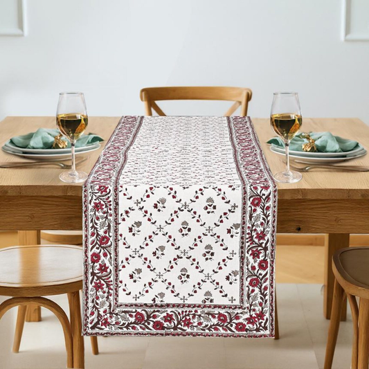 Dining table set with a floral table runner, glasses, and plates.