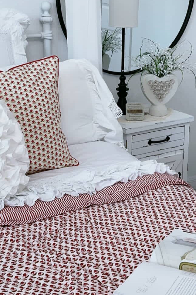 Bedroom with white bedding, red and white patterned blanket, and round mirror.