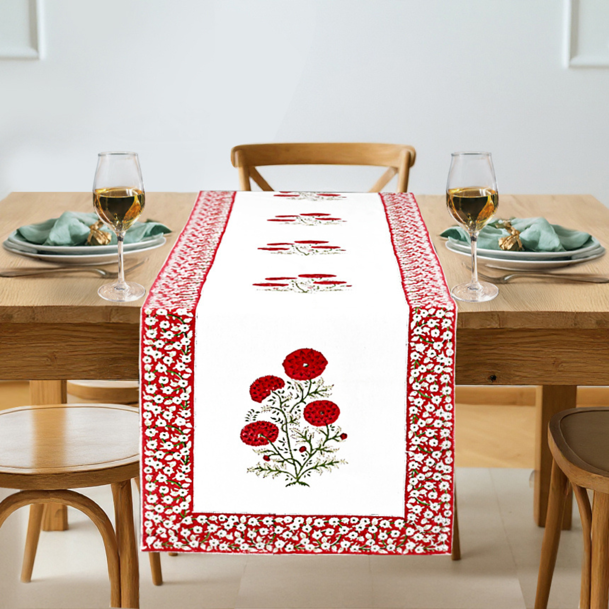 Dining table set with a red and white floral table runner, glasses, and plates.