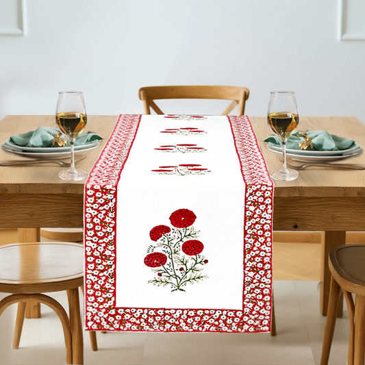 Dining table set with a red and white floral table runner, glasses, and plates.