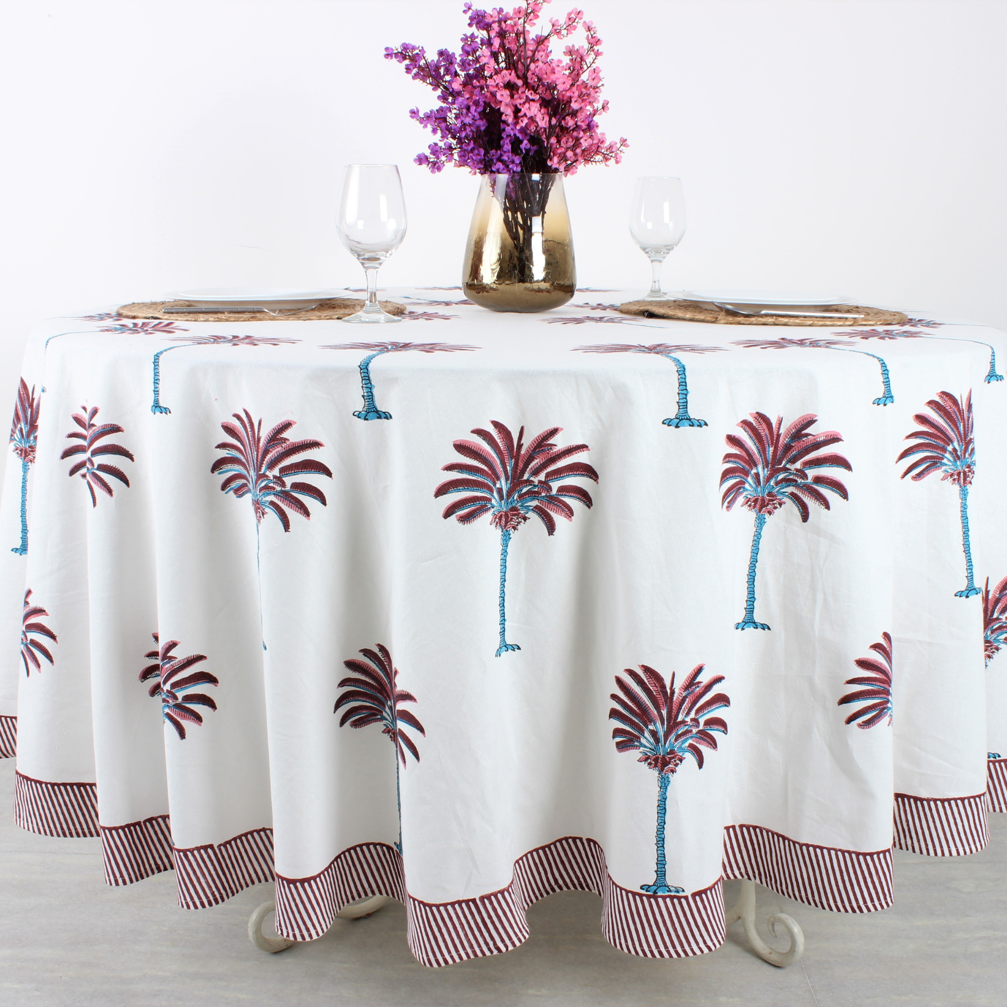 Tablecloth with palm tree design on a table set with glasses and a vase of flowers.